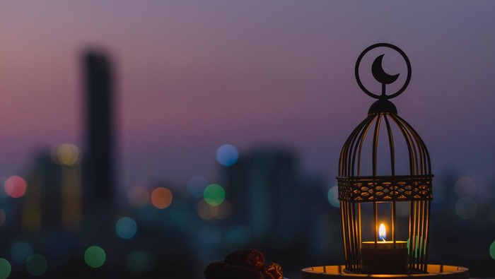 Lantern that have moon symbol on top and small plate of dates fruit with dusk sky and city bokeh light background for the Muslim feast of the holy month of Ramadan Kareem.