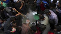 Warga mengantre mengambil hidangan berbuka puasa di sebuah gang sempit di Shijaiya dekat perbatasan Gaza, Palestina, Rabu (6/4/2022) waktu setempat. Hidangan yang disajikan adalah semangkuk sup dan bubur gandum.  