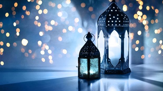 Couple of glowing Moroccan ornamental lanterns on the table. Greeting card, invitation for Muslim holy month Ramadan Kareem, festive blue night background with glittering golden bokeh lights.