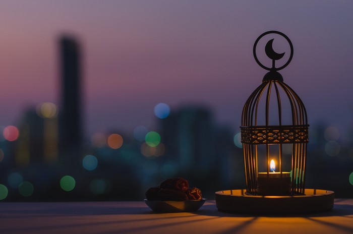 Lantern that have moon symbol on top and small plate of dates fruit with dusk sky and city bokeh light background for the Muslim feast of the holy month of Ramadan Kareem.