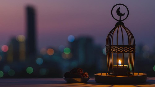 Lantern that have moon symbol on top and small plate of dates fruit with dusk sky and city bokeh light background for the Muslim feast of the holy month of Ramadan Kareem.