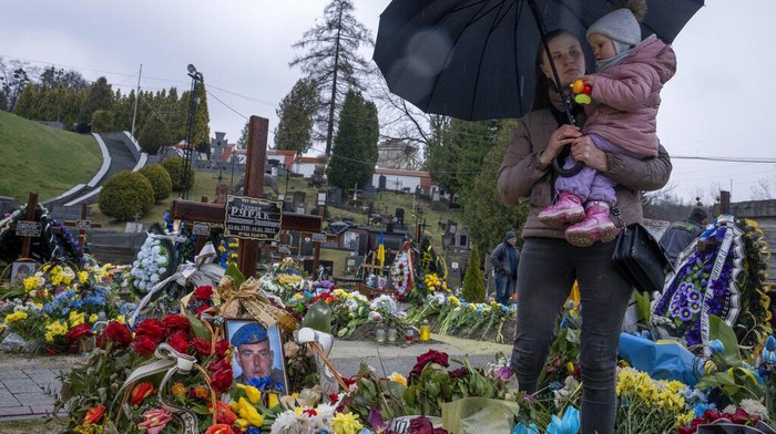 Tetiana Rurak, 25-year-old widow Oleksandra Rurak, visits her soldier husband Volodymyr Rurak's, grave with her one and a half year old daughter, after he was killed in action, at the Lychakiv cemetery, in Lviv, western Ukraine, Tuesday, April 5, 2022. (AP Photo/Nariman El-Mofty)