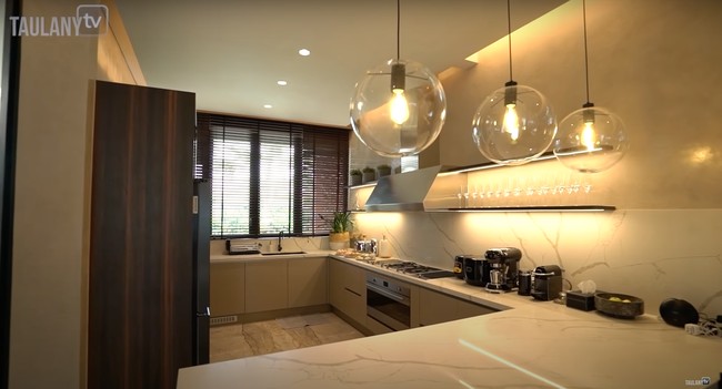 Bagian dalam rumah Maia Estianty juga dilengkapi dengan dapur yang tak kalah menawan. Dengan dominasi warna coklat dan lampu berwarna kekuningan, dapur di rumah Maia itu tampak begitu elegan. Ketiga lampu gantung yang terpasang juga menambah estetika ruangan. Foto: YouTube/Taulany TV