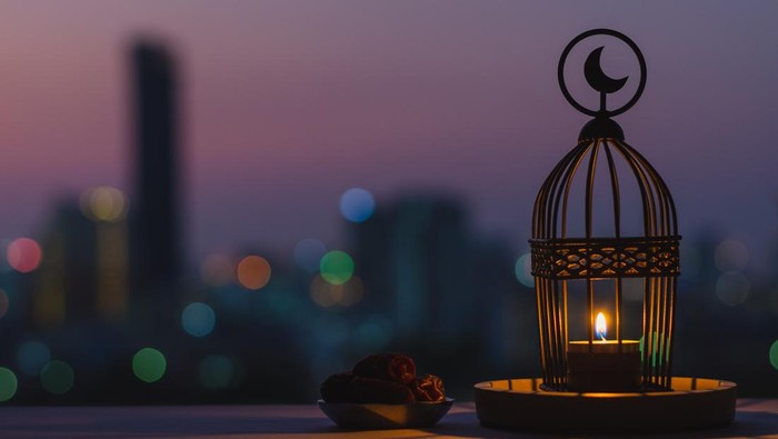 Lantern that have moon symbol on top and small plate of dates fruit with dusk sky and city bokeh light background for the Muslim feast of the holy month of Ramadan Kareem.