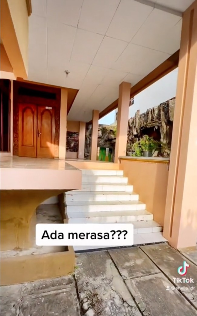 Jika dilihat, desain rumah yang satu ini memang terlihat unik dan berbeda dari rumah-rumah pada umumnya. Tembok samping bagian luar rumah tampak didesain menyerupai bebatuan. Rumahnya pun terlihat tinggi, perlu menaiki tangga terlebih dahulu untuk masuk ke dalam rumah. Foto: TikTok/@shella_dr