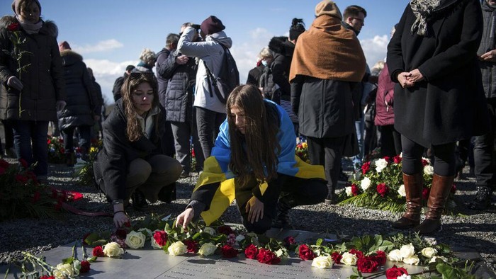 Ukrainian student from Mykolaiv, Yana Alimova, center, places a flower during a wreath laying ceremony marking the 77th anniversary of the liberation of the Nazi concentration camp Buchenwald near Weimar, Germany, Sunday, April 10, 2022. On April 11, 1945 the US Army liberated the concentration camp Buchenwald. (AP Photo/Steffi Loos)