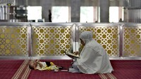 Perempuan tadarus Al-Quran sambil menjaga bayi di Masjid Itiqlal, Jakarta, Selasa (5/4/2022).  (AP Photo/Tatan Syuflana)