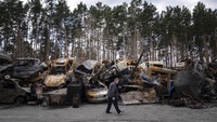 Seorang pria berjalan melewati tempat penyimpanan kendaraan yang hancur di pinggiran Kyiv, Ukraina, Senin (11/4/2022). AP Photo/Evgeniy Maloletka.