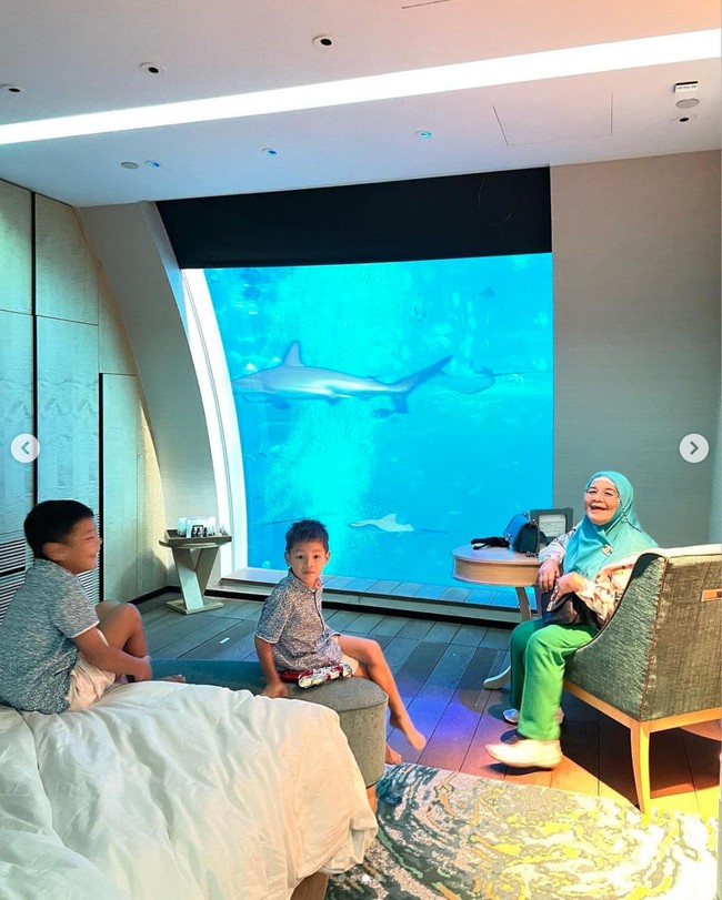 Pemandangan bawah laut itu langsung menghadap ke tempat tidur di dalam kamar hotel. Di sampingnya juga tampak disediakan meja dan kursi untuk duduk dan menikmati pemandangan akuarium bawah laut. Terlihat ibu Titi Kamal dan anak-anaknya begitu senang menghabiskan waktu di dalam kamar hotel tersebut. Foto: Instagram/@titi_kamall