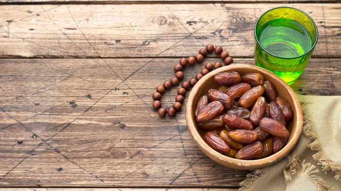 Dried dates fruits and a glass of water on a wooden table. Traditional fast breaking, Muslims evening meal during holy Ramadan