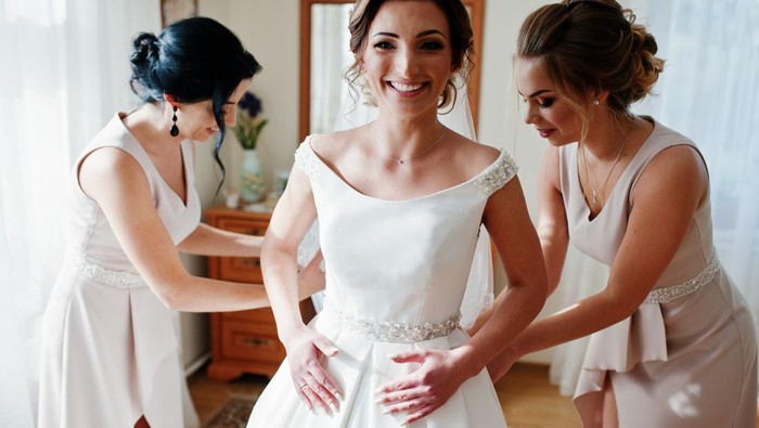 Bridesmaids helping gorgeous bride to dress up and get ready for her wedding ceremony.