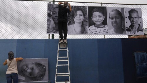 People visit the photographic installation Inside Out, in the San Blas community of Petare, in Caracas, Venezuela, Tuesday, April 12, 2022. The initiative created by the French street artist Jean René, better known as JR, in an effort to overcome the stigma of violence that accompanies the neighborhood.  (AP Photo/Ariana Cubillos)