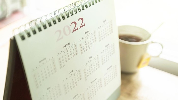 Paper desktop calendar 2022 schedule with tea cup on wooden desk