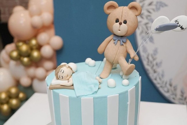 Kue baby shower milik Jessica Iskandar pun terlihat cukup unik dan lucu. Kue berwarna biru itu tampak dihiasi dengan bentuk beruang yang membawa balon dan seorang anak laki-laki yang tengah tertidur.  Foto: Instagram