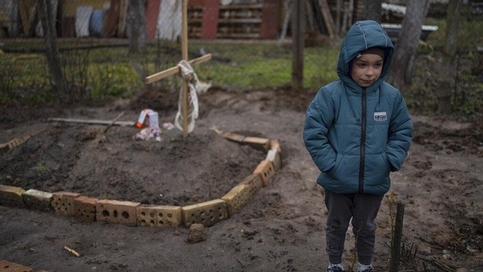 Potret Anak-anak yang Selamat dari Kengerian di Kota Bucha FILE - In the courtyard of their house, Vlad, 6, stands near the grave of his mother, who died, on the outskirts of Kyiv, Ukraine, Monday, April 4, 2022. Vlad's mother died last month when the family was forced to shelter in a basement during the occupation by the Russian army. The family still doesn't know what illness caused her death. (AP Photo/Rodrigo Abd)