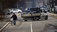 Warga menuntun sepedanya melintasi mobil bak yang berisi kantong jenazah korban perang di Bucha, Ukraine, Senin (11/4/2022). Kendaraan pribadi maupun bermotor nyaris tidak terlihat di kota-kota yang hancur terkena rudal. (AP Photo/Rodrigo Abd)