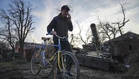 Pengendara menuntun sepeda di depan tank Rusia yang hancur di Chernihiv, Ukraina, Kamis (7/4/2022). Sepeda tersebut dicat warna biru dan kuning seperti warna bendera Ukraina. (AP Photo/Evgeniy Maloletka)