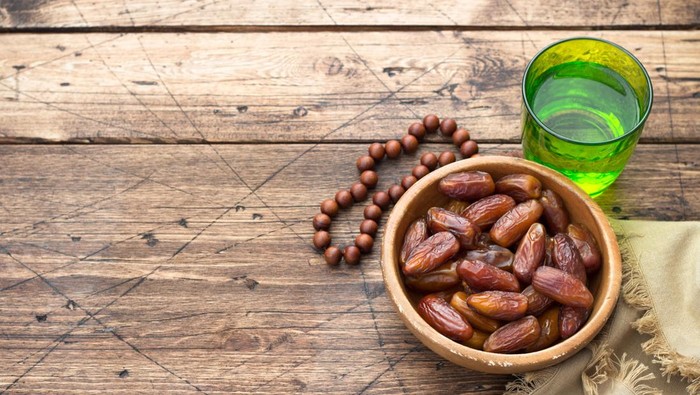 Dried dates fruits and a glass of water on a wooden table. Traditional fast breaking, Muslims evening meal during holy Ramadan