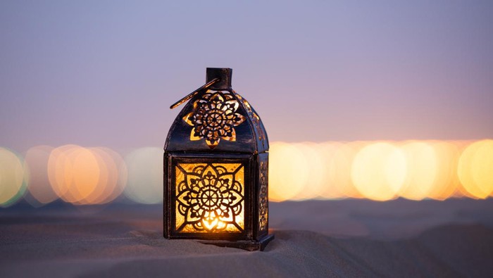 Traditional ornamental arabic lantern with a burning candle in desert after sunset during blue hour. Festivel greeting card for Ramadan Kareem and Ramadan Mubarak. Dubai, UAE.