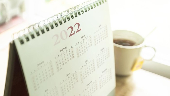 Paper desktop calendar 2022 schedule with tea cup on wooden desk