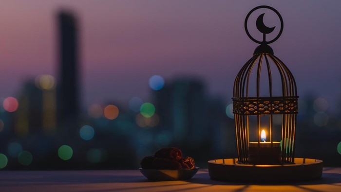 Lantern that have moon symbol on top and small plate of dates fruit with dusk sky and city bokeh light background for the Muslim feast of the holy month of Ramadan Kareem.