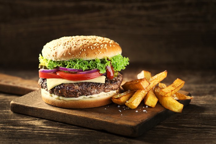 Delicious Hamburger with cheese and french fries on wooden table and dark background