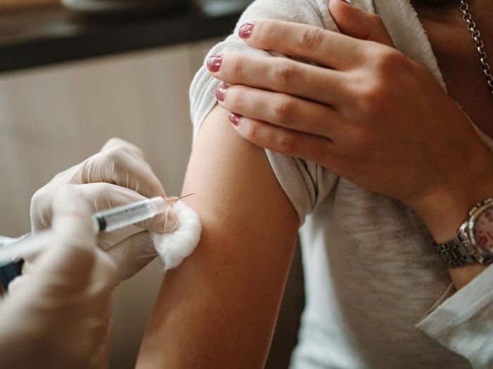 Young doctor giving COVID 19 vaccine to young woman at home