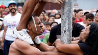 Seorang pria tampak menahan beban rekannya saat berpartisipasi dalam permainan panjat tiang berminyak.