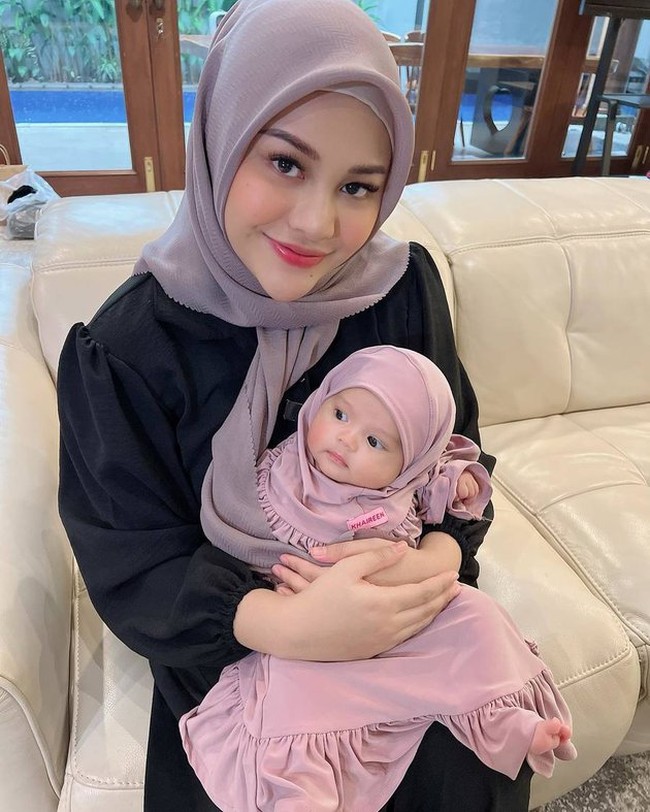 Sambil dipangku Aurel Hermansyah, baby Ameena yang mengenakan setelan hijab berwarna ungu itu tampil menggemaskan. Penampilan baby Ameena saat mengenakan hijab pun diunggah ke Instagram dan berhasil bikin netizen heboh karena ikut merasa gemas. Foto: Instagram