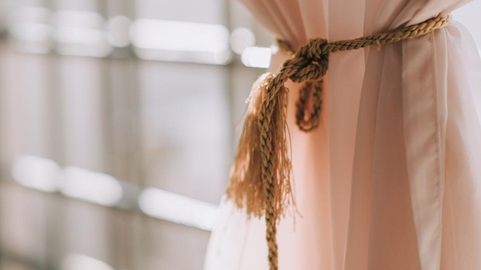 a curtain tied up with sunlight from outside window frame