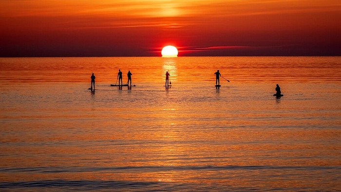 Paddle boarders tour the calm Baltic Sea in Timmendorfer Strand northern Germany as the sun rises on a cold Monday, morning, April 18, 2022. (AP Photo/Michael Probst)