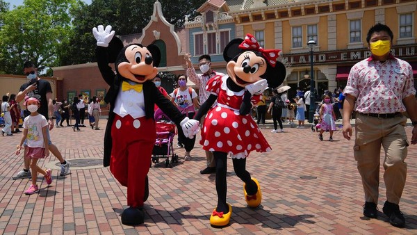 Staf mengenakan masker wajah memimpin karakter ikonik Mickey dan Minnie Mouse di Disneyland Hong Kong. Taman hiburan tetap sama dalam atraksinya, tetapi hanya mengizinkan pengunjung hingga 50% dari kapasitasnya.
