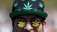Seorang pria mengenakan topi dan kacamata bergambar ganja saat mengikuti aksi demo.