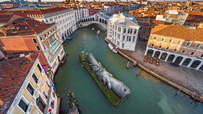 An aerial view shows an artwork by French-Swiss artist Saype called 'Beyond Walls' on a floating barge, part of a series of interlocked hands as part of a project creating a spray-painted 'human chain' across the world to encourage humanity and equality, in Venice, Italy, April 17, 2022. Picture taken with a drone, April 17, 2022. Valentin Flauraud for Saype/Handout via REUTERS THIS IMAGE HAS BEEN SUPPLIED BY A THIRD PARTY. MANDATORY CREDIT. NO RESALES. NO ARCHIVES