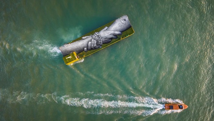 Potret Lukisan Raksasa 'Rantai Manusia' Mengapung di Venesia, Italia An aerial view shows an artwork by French-Swiss artist Saype called 'Beyond Walls' on a floating barge, part of a series of interlocked hands as part of a project creating a spray-painted 'human chain' across the world to encourage humanity and equality, in Venice, Italy, April 17, 2022. Picture taken with a drone, April 17, 2022. Valentin Flauraud for Saype/Handout via REUTERS THIS IMAGE HAS BEEN SUPPLIED BY A THIRD PARTY. MANDATORY CREDIT. NO RESALES. NO ARCHIVES