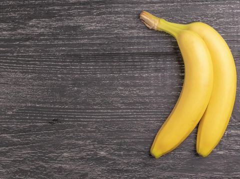 Two ripe yellow bananas on the old rough scratched wooden boards background surface. Top view