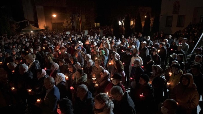 An Orthodox worshiper holds a candle, seen through a plastic panel, during the Easter religious service at the Brancusi Parish Church in Bucharest, Romania, Sunday, April 24, 2022. The religious service was also attended by dozens of Ukrainian refugees living in a social center belonging to the church. (AP Photo/Andreea Alexandru)