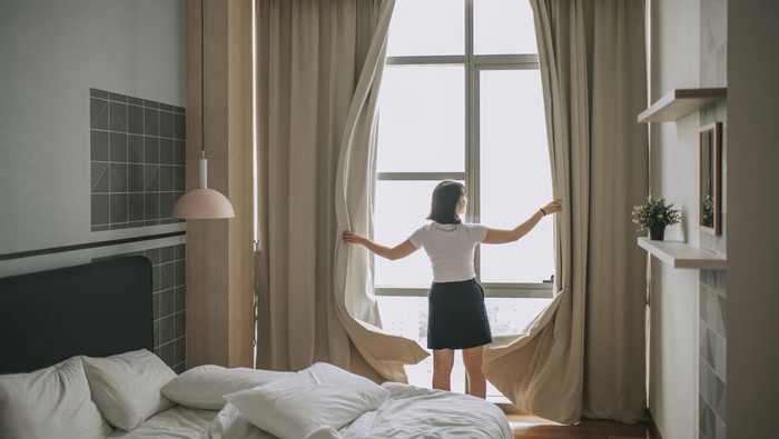rear view asian chinese teenage girl open curtain of her bedroom in the morning