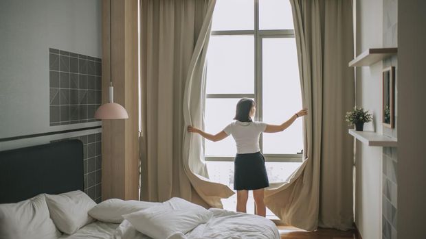 rear view asian chinese teenage girl open curtain of her bedroom in the morning