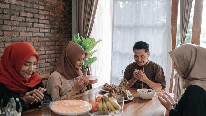 Jadwal buka puasa asian muslim people praying before having their food in dining room together for break fasting