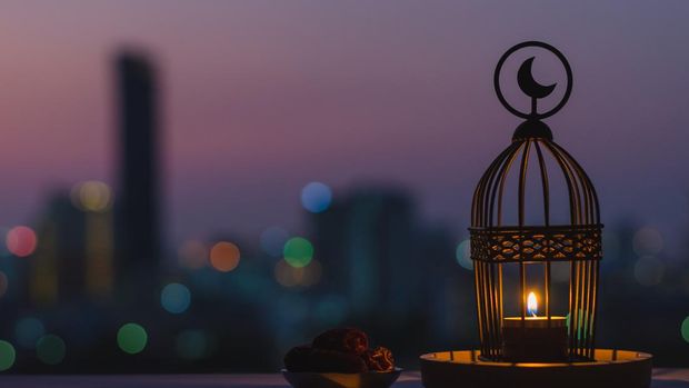 Lantern that have moon symbol on top and small plate of dates fruit with dusk sky and city bokeh light background for the Muslim feast of the holy month of Ramadan Kareem.