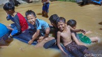 Anak-anak tampak bermain di air banjir yang kotor.