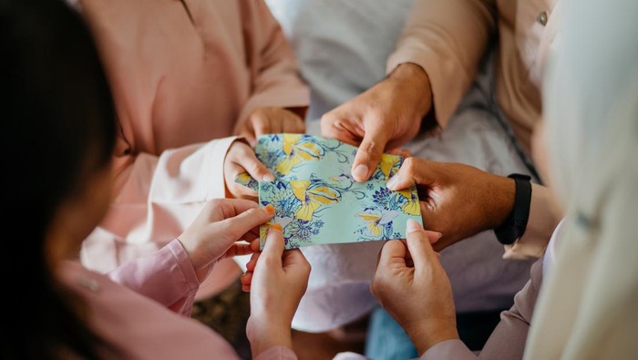 Malay Muslim parents in traditional clothings giving gift of money to their children during Hari Raya Aidilfitri celebration