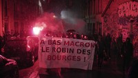 Demonstran membawa poster berisi protes kepada Emmanuel Macron yang kembali mencalonkan diri menjadi Presiden Prancis, Minggu (24/4/2022). (AP Photo/Laurent Cipriani).