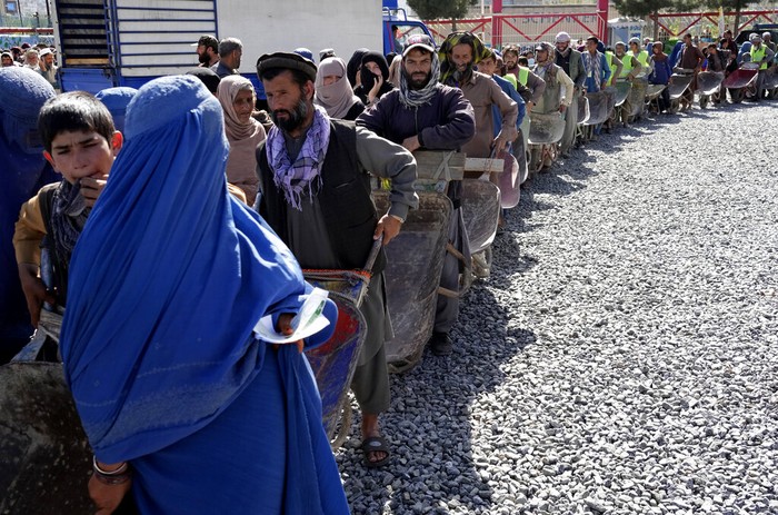 A Taliban fighter stands guard as people receive food rations distributed by a Saudi humanitarian aid group, in Kabul, Afghanistan, Monday, April 25, 2022. (AP Photo/Ebrahim Noroozi)