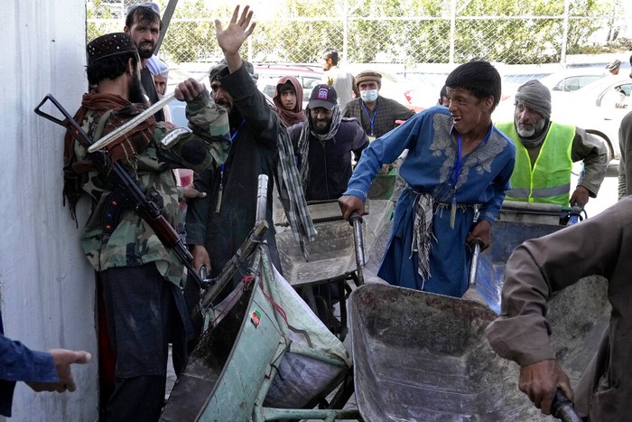 A Taliban fighter stands guard as people receive food rations distributed by a Saudi humanitarian aid group, in Kabul, Afghanistan, Monday, April 25, 2022. (AP Photo/Ebrahim Noroozi)