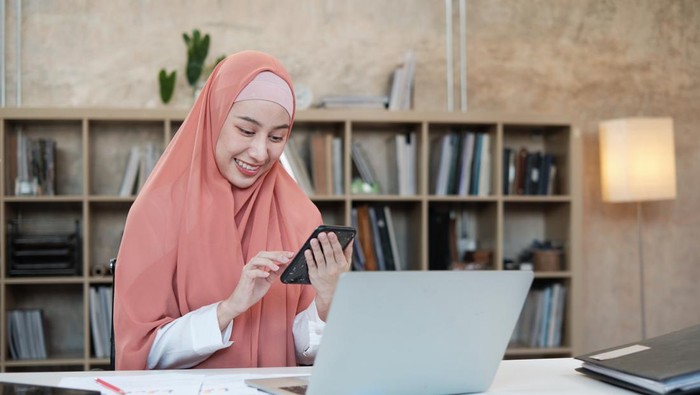Ilustrasi wanita hijab mengirim ucapan Idul Fitri lewat ponsel