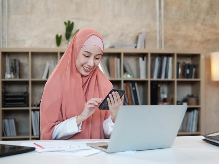 Ilustrasi wanita hijab mengirim ucapan Idul Fitri lewat ponsel