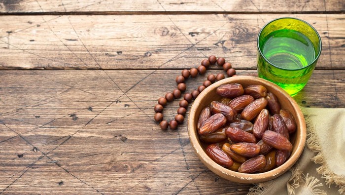 Dried dates fruits and a glass of water on a wooden table. Traditional fast breaking, Muslims evening meal during holy Ramadan