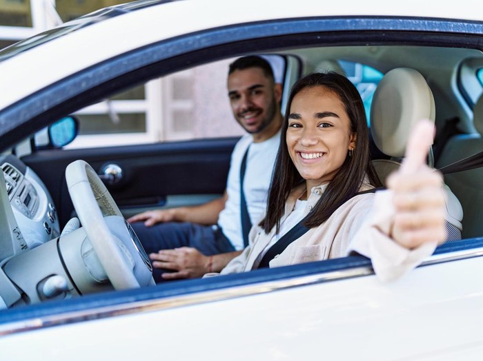 Young hispanic couple smiling happy driving car at the city. Girl doing ok gesture with thumb up.